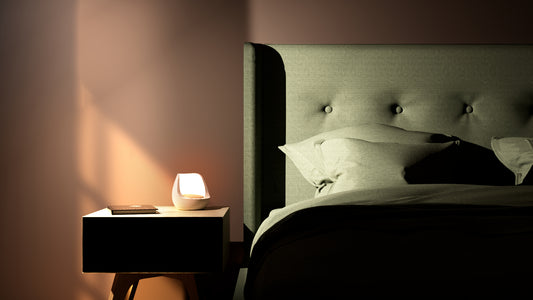 Bildet viser en Wake-Up Light på et sort nattbord ved siden av en seng med grønt sengetøy