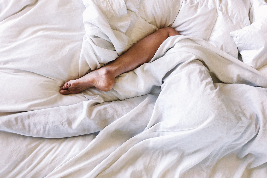 Hvordan sovne fort? Bilde av et ben som stikker ut mellom hvitt og delikat sengetøy.